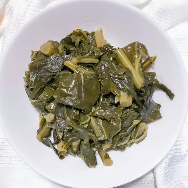 A white bowl filled with dark green, cooked collard greens, a classic soul food side dish.